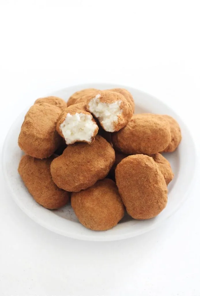 A plate of Irish potato candies coated in cinnamon, with one candy bitten to reveal a creamy coconut filling, perfect for traditional Irish desserts or St Patrick's Day celebrations.