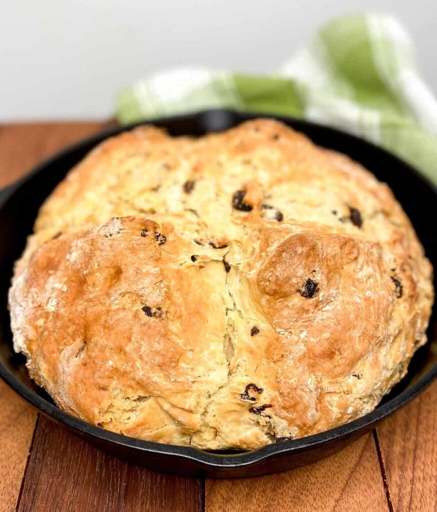 Golden-brown Irish soda bread baked in a cast iron skillet, studded with raisins and featuring a rustic texture—perfect for St. Patrick's Day food ideas and traditional Irish recipes.