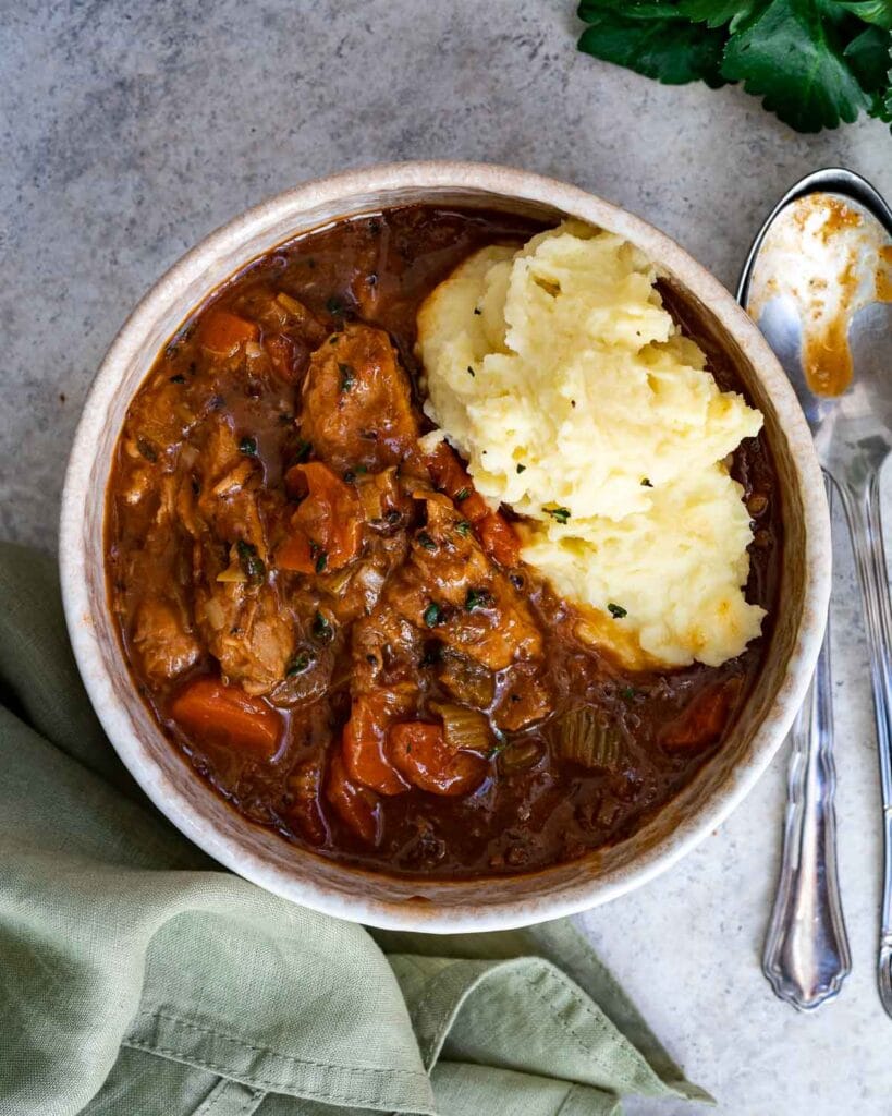 Bowl of hearty beef stew with tender chunks of meat, vegetables, and a rich gravy, served alongside creamy mashed potatoes—an ideal comfort food made from leftovers recipes.