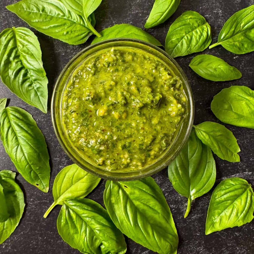 Close-up of a jar of vibrant green pesto surrounded by fresh basil leaves—a versatile and flavorful sauce that’s perfect for leftovers recipes or enhancing your favorite dishes.