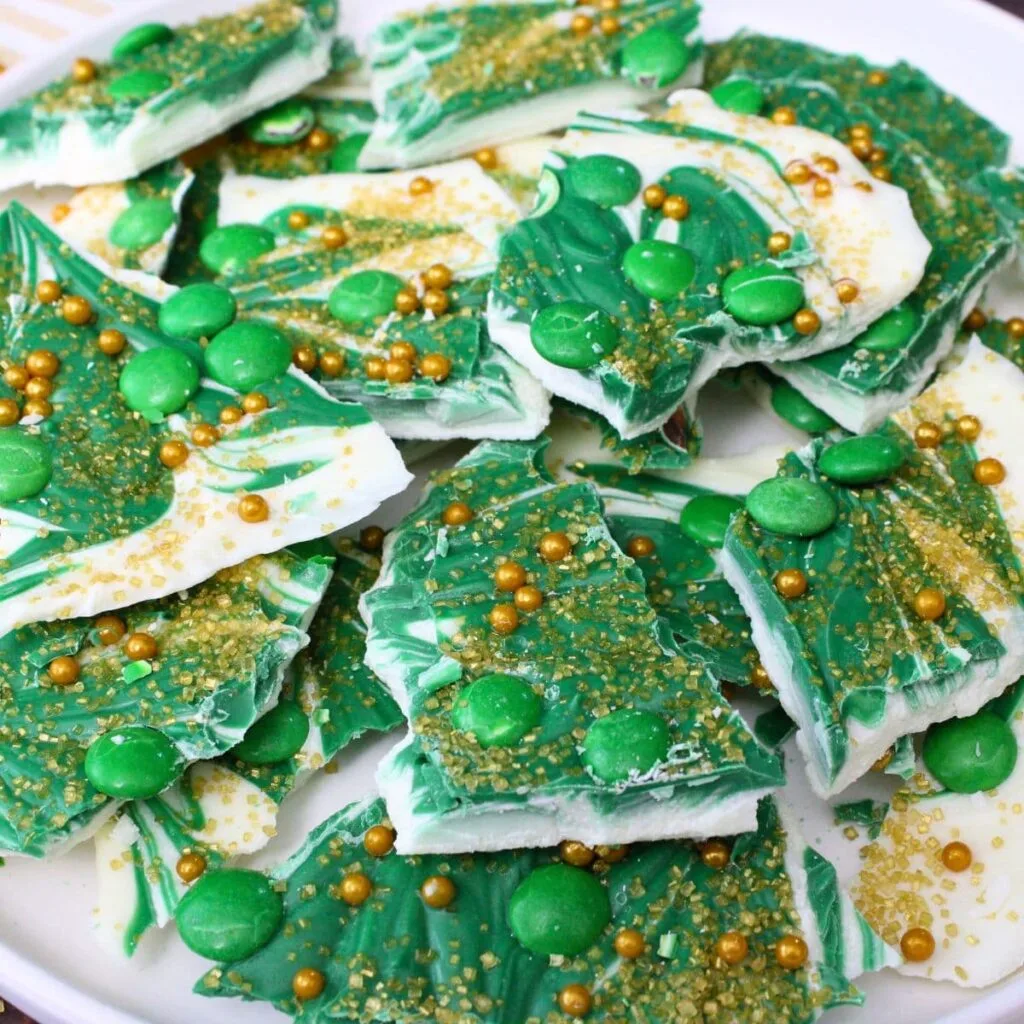 Vibrant green and white swirled candy bark topped with green candies, gold sprinkles, and edible glitter, perfect for St. Patrick's Day celebrations or Irish-themed desserts.