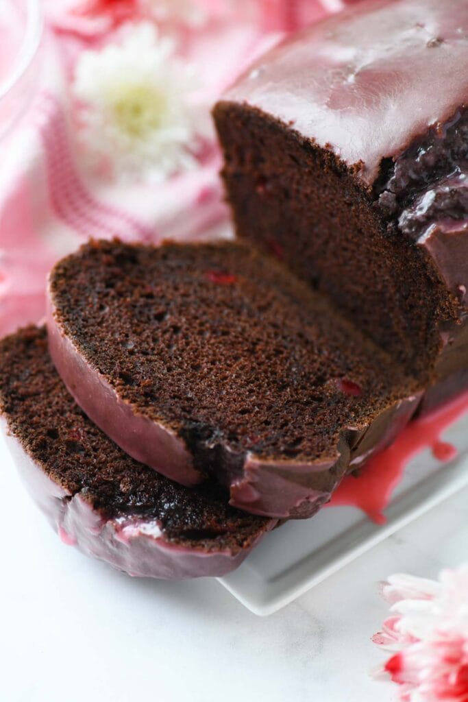 Close-up of a chocolate loaf cake with a glossy glaze, sliced to reveal its moist texture, set against a romantic backdrop, making it an elegant option for Valentine's Cake Ideas.