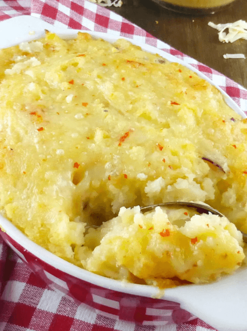 Close-up of a creamy baked mashed potato casserole topped with melted cheese and red chili flakes, served in a dish—a comforting and flavorful option for creative leftovers recipes.