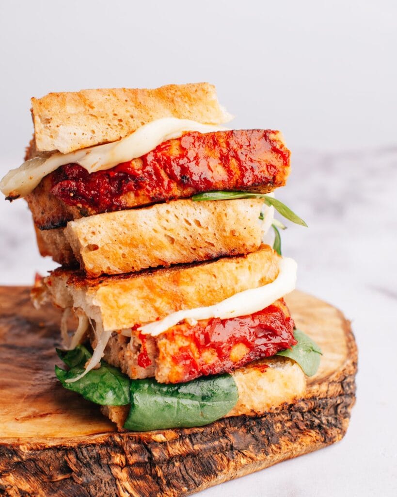 Stacked meatloaf sandwiches with crispy bread, juicy slices of glazed meatloaf, fresh spinach, and melted cheese—a mouthwatering way to repurpose leftovers into a hearty meal.