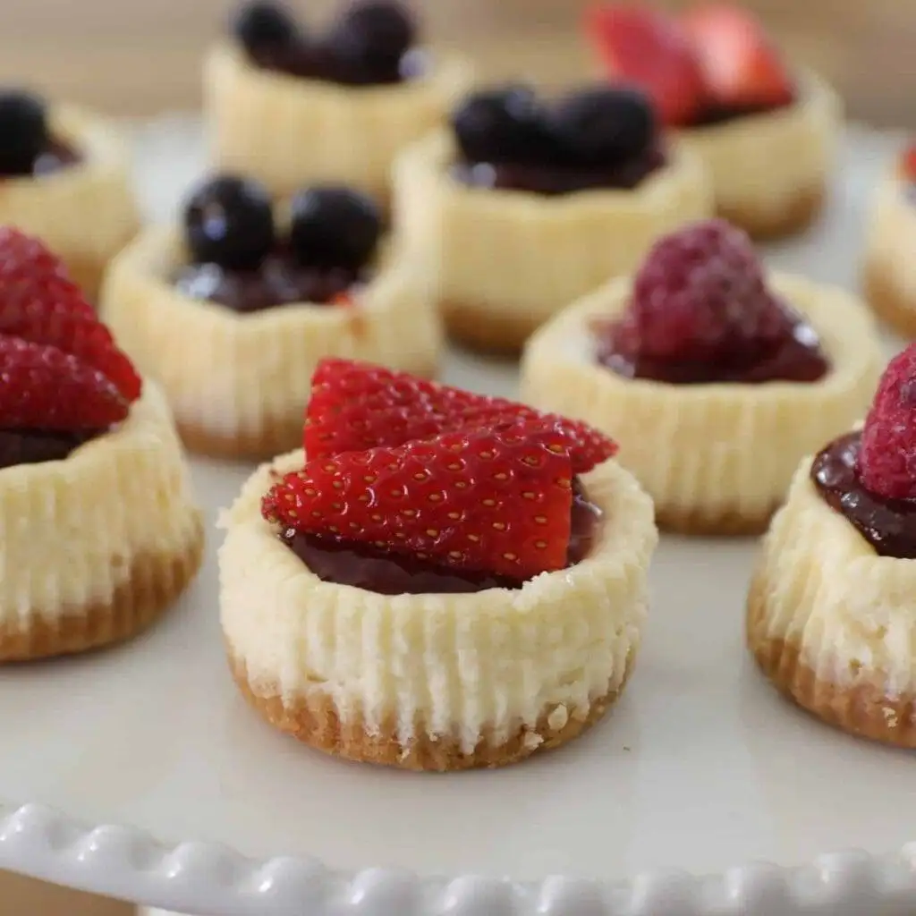Mini cheesecakes topped with fresh strawberries, blueberries, and raspberries, arranged on a white platter, making them a delightful option for romantic desserts for two or a sweet treat for any occasion.
