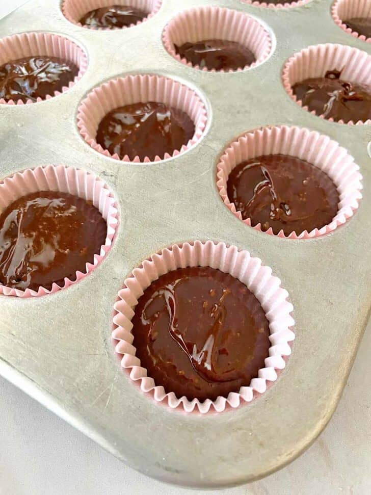 Close-up of a muffin tin filled with pink cupcake liners, each holding rich chocolate batter, perfect for baking Valentine's Cake Ideas with a personal touch.