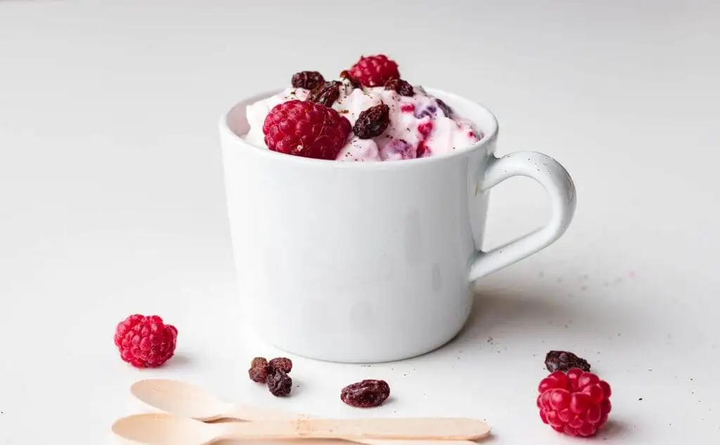 A white mug filled with creamy yogurt topped with fresh raspberries and dried cranberries, offering a simple yet elegant option for romantic desserts for two or a wholesome treat.