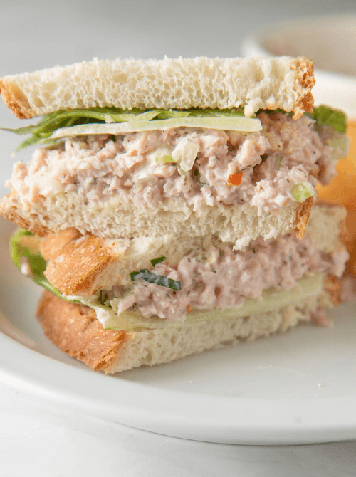 Thick ham salad sandwich with fresh lettuce and soft bread, perfect for quick meals or lunch on the go, served on a white plate.