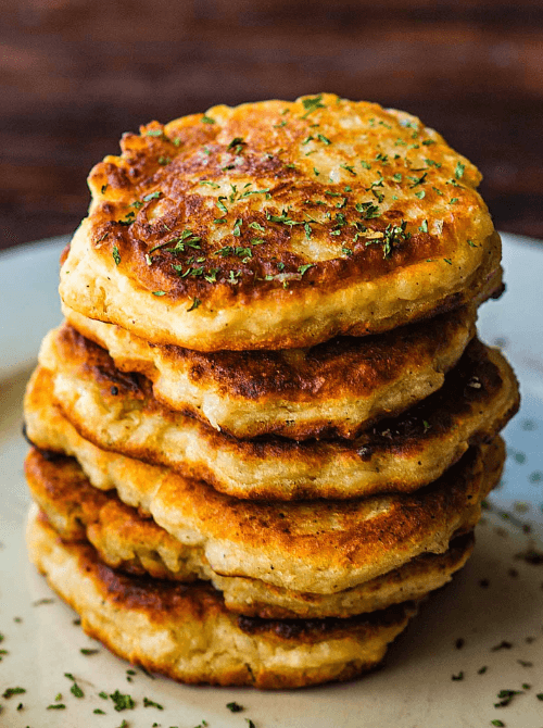 Stack of crispy, golden-brown potato cakes garnished with fresh herbs, made from leftover mashed potatoes—perfect for creative leftovers recipes that are both delicious and budget-friendly.