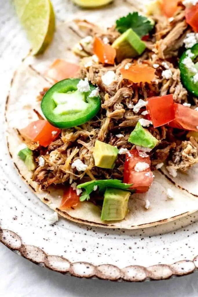 Close-up of a taco topped with shredded pork, diced avocado, tomatoes, jalapeño slices, and crumbled cheese, served on a soft tortilla—a vibrant and delicious option for leftovers recipes.