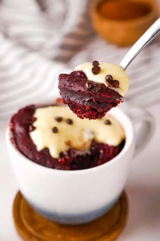A rich red velvet mug cake topped with cream cheese frosting and chocolate chips, a quick and indulgent option for romantic desserts for two.