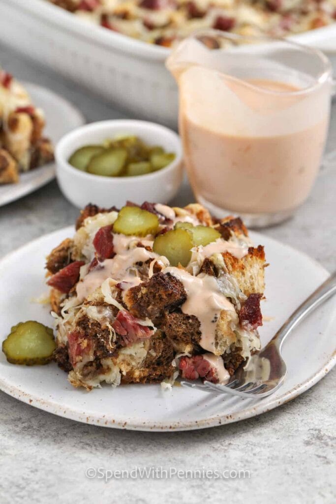 Reuben casserole topped with pickles and creamy sauce, served alongside extra pickles and dressing, ideal for St. Patrick's Day food ideas and Irish-inspired recipes with a comforting twist.