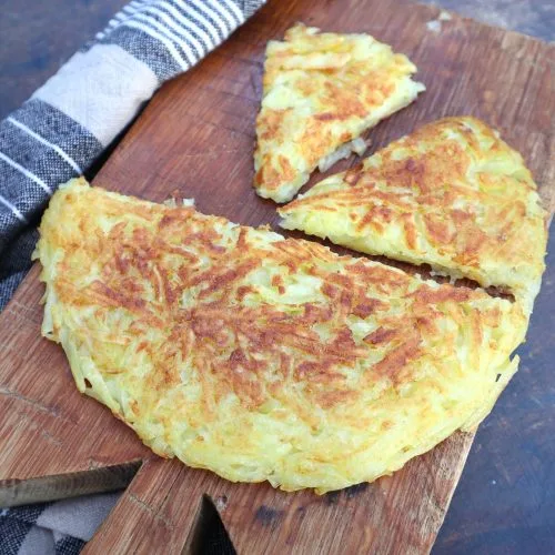 Golden, crispy hash brown patty cut into wedges and served on a wooden board, perfect as a simple and crowd-pleasing Super Bowl food idea for game day brunch or snacks.