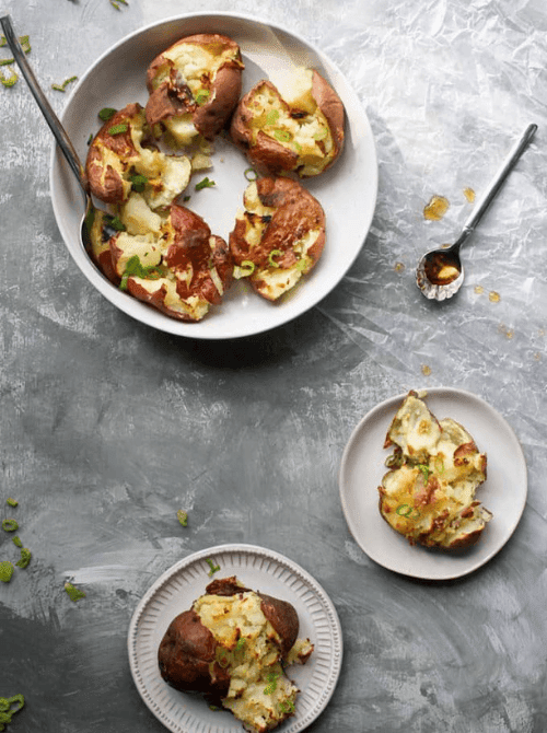 Salt and vinegar smashed potatoes topped with scallions, served on white plates—tangy and crispy addition to Super Bowl food ideas.