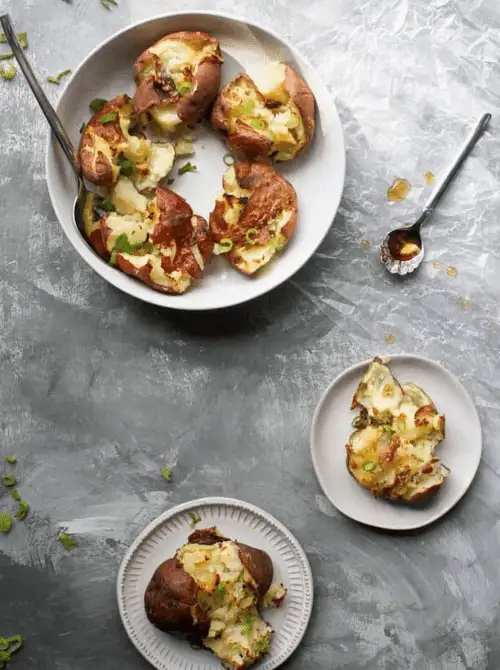 Salt and vinegar smashed potatoes topped with scallions, served on white plates—tangy and crispy addition to Super Bowl food ideas.