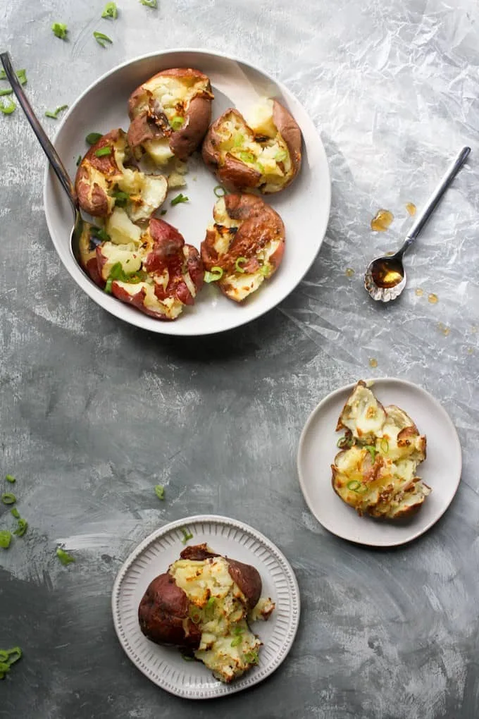 Smashed red potatoes topped with melted cheese, green onions, and crispy bacon, served on white plates. A simple and flavorful Super Bowl food idea for game day appetizers.