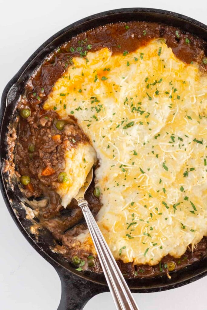 Skillet of homemade shepherd's pie with a savory meat and vegetable filling topped with creamy mashed potatoes and melted cheese, garnished with parsley—perfect for St. Patrick's Day food ideas and traditional Irish recipes.