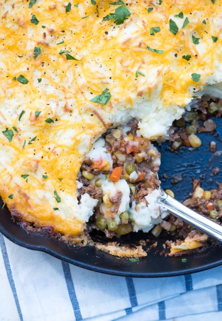 Close-up of a skillet filled with classic shepherd's pie, featuring a hearty meat and vegetable filling topped with golden mashed potatoes and melted cheese, garnished with fresh parsley—perfect for St. Patrick's Day food ideas and Irish-inspired recipes.