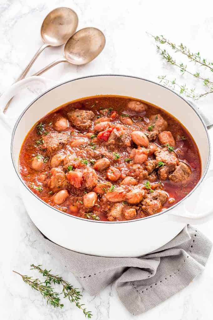 White pot filled with hearty lamb and bean stew in a rich tomato base, garnished with fresh thyme sprigs—an ideal dish for St. Patrick's Day food ideas and comforting Irish-inspired recipes.