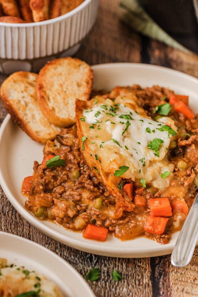 Plate of deconstructed shepherd's pie with a rich meat and vegetable filling topped with melted cheese and garnished with fresh parsley, served with slices of toasted bread—perfect for St. Patrick's Day food ideas and Irish-inspired recipes.