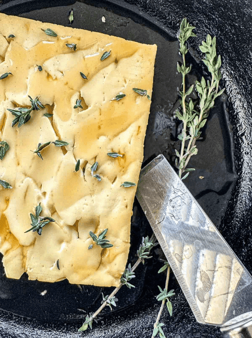 Smoked feta cheese topped with fresh thyme and drizzled with honey, served in a cast iron skillet—an elevated twist for Super Bowl food ideas.