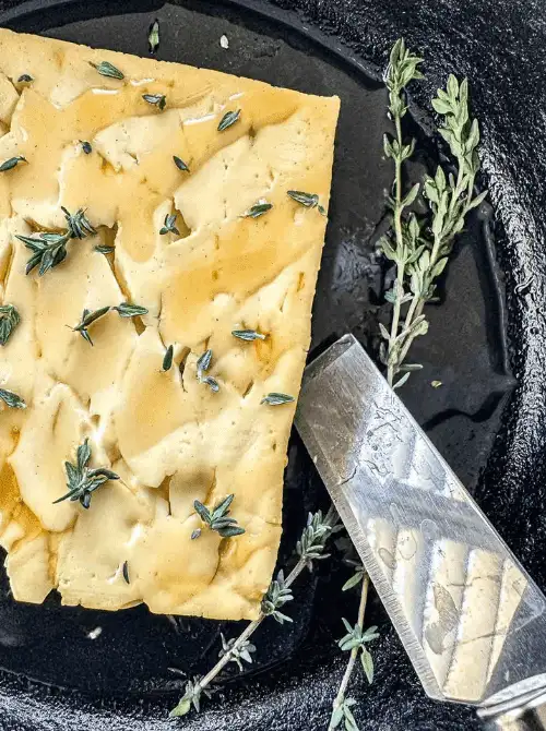 Smoked feta cheese topped with fresh thyme and drizzled with honey, served in a cast iron skillet—an elevated twist for Super Bowl food ideas.