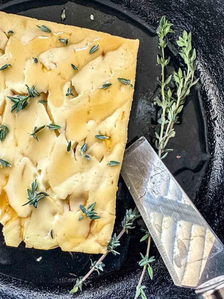 A rustic block of cheese garnished with fresh thyme, served in a black skillet. Perfect for Super Bowl food ideas, this appetizer brings a touch of elegance to the game day spread.