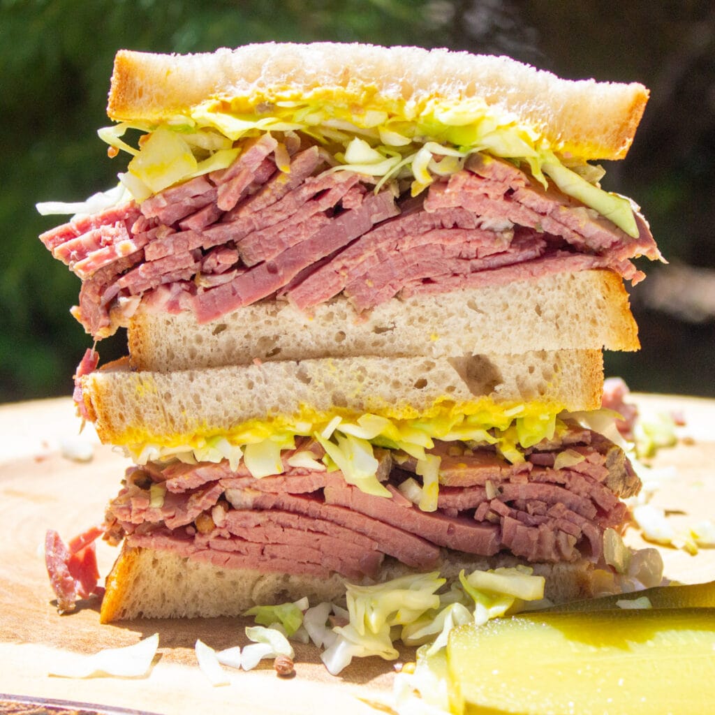 Stacked corned beef sandwich with layers of tender beef, shredded cabbage, and mustard on rye bread, served with pickle slices—perfect for St. Patrick's Day food ideas and Irish-inspired recipes.