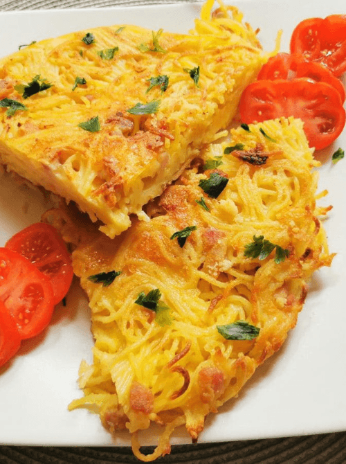 Golden, crispy spaghetti frittata slices garnished with fresh parsley, served alongside sliced cherry tomatoes—a creative and delicious way to repurpose leftover pasta in unique recipes.