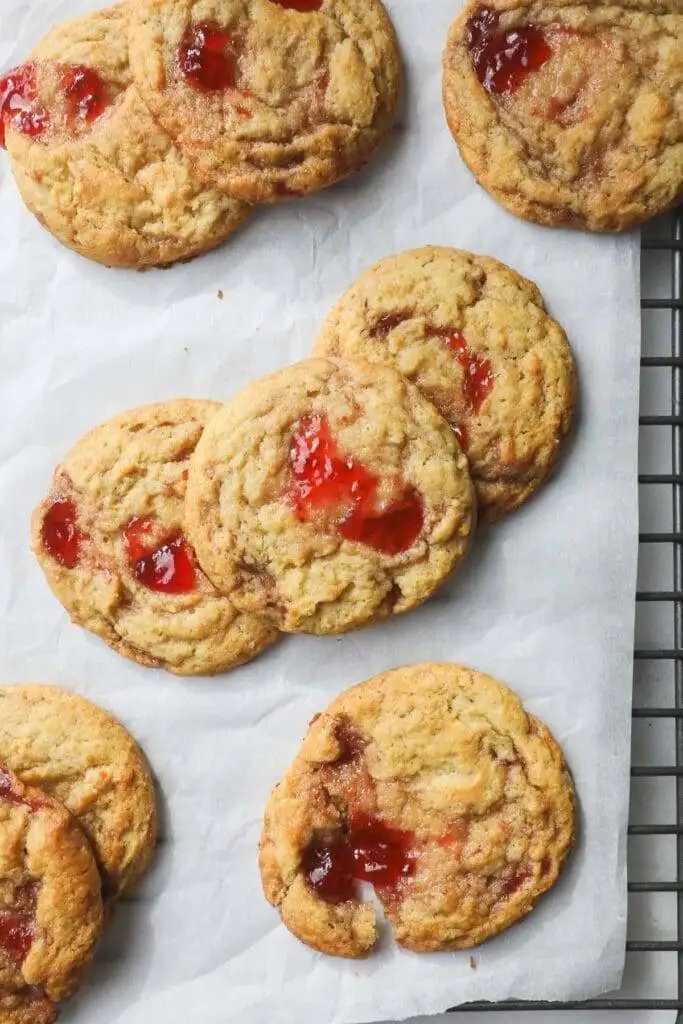 Golden-brown heart cookies with swirls of vibrant red jam baked into the surface, arranged on a sheet of parchment paper for a warm and inviting presentation.