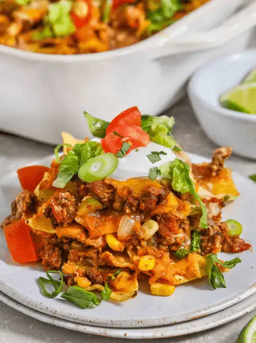 Layered taco bake with ground beef, cheese, corn, and tomatoes, topped with sour cream, green onions, and lettuce—served hot for an easy game day dinner.
