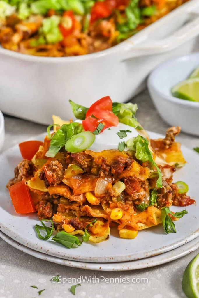 A slice of cheesy taco casserole layered with seasoned ground beef, corn, and tortilla pieces, topped with sour cream, green onions, lettuce, and diced tomatoes. A flavorful and easy Super Bowl food idea for game day feasting.