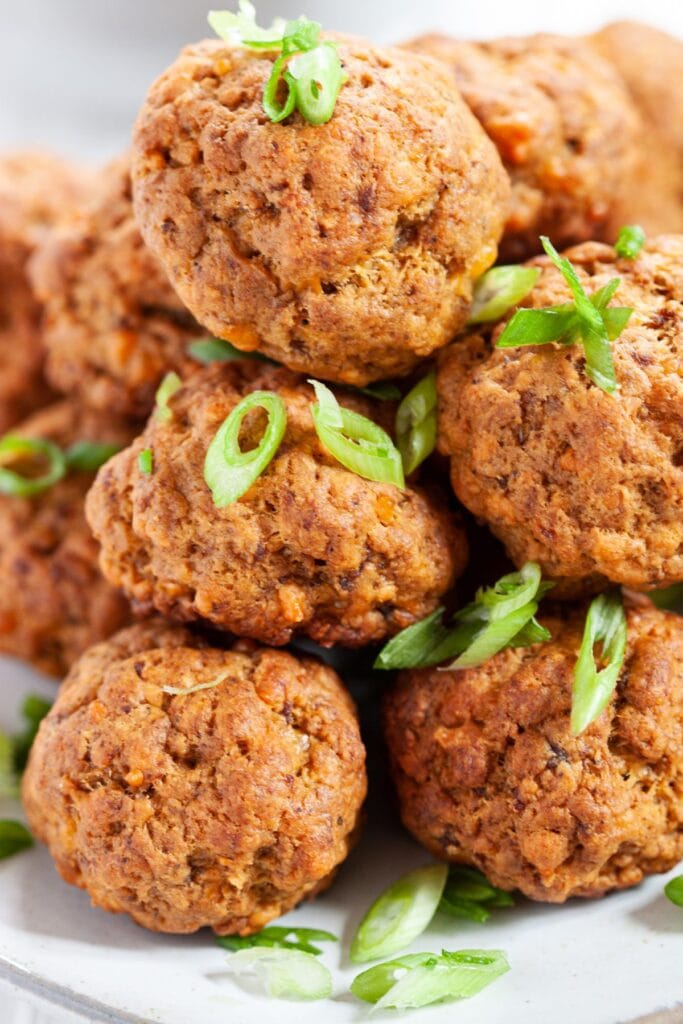A plate of golden-brown baked meatballs garnished with freshly sliced green onions. These hearty and flavorful bites make a perfect Superbowl appetizer for meat lovers.