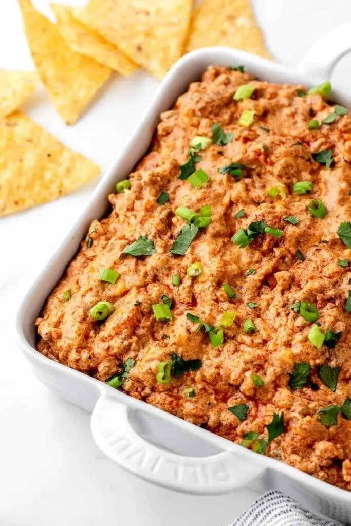 Spicy and flavorful taco dip garnished with fresh herbs and green onions, served alongside tortilla chips—an irresistible choice for the best party dips lineup.