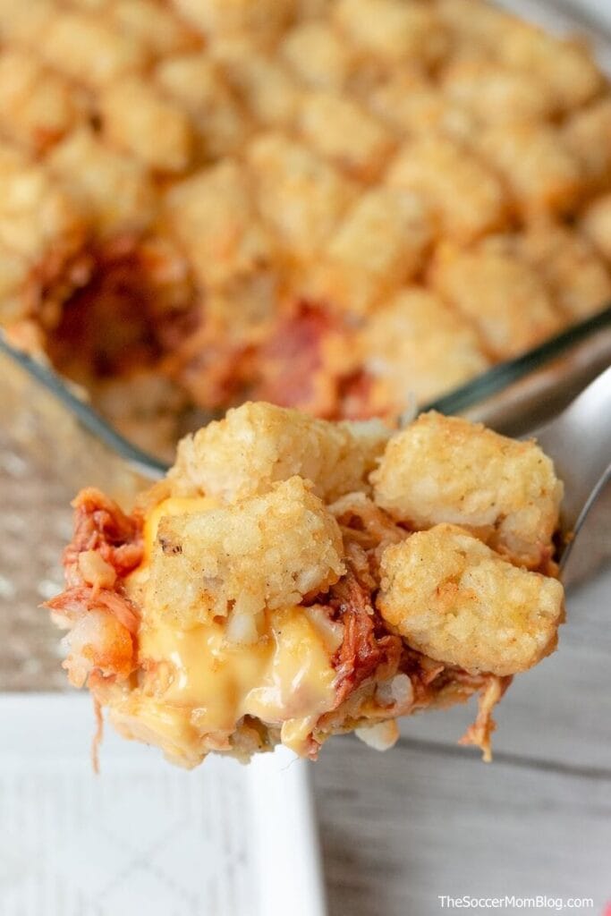 Cheesy tater tot casserole with leftover pulled pork, featuring golden crispy tots and melted cheese, served from a glass baking dish.