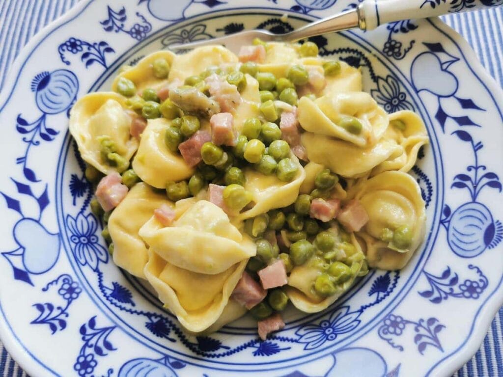 Plate of creamy tortellini mixed with peas and diced ham, served in a rich sauce—a quick and delicious meal idea for creative leftovers recipes.