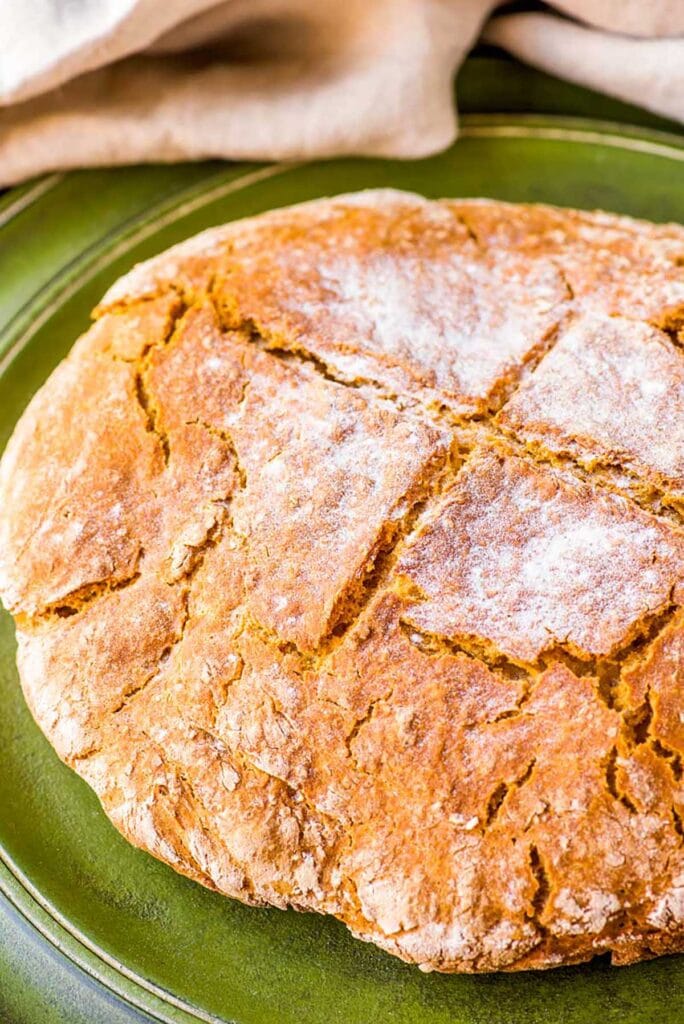 Golden, rustic Irish soda bread with a flour-dusted crust and traditional cross scoring, served on a green plate—perfect for St. Patrick's Day food ideas and authentic Irish recipes.