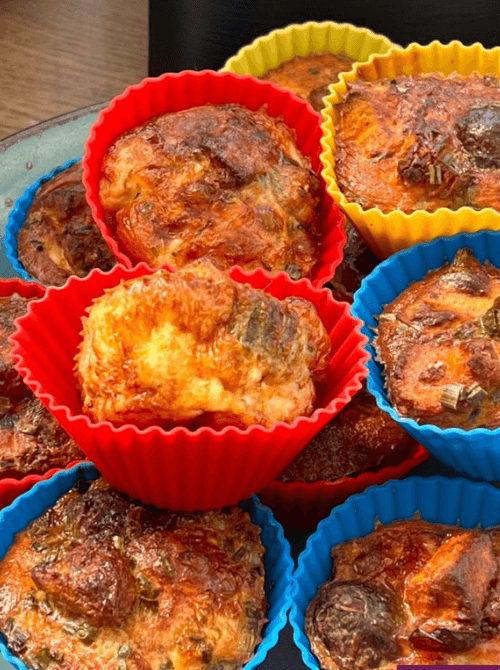 Colorful silicone cups filled with golden-brown mini quiches, packed with herbs and cheese—a perfect grab-and-go option for creative leftovers recipes.