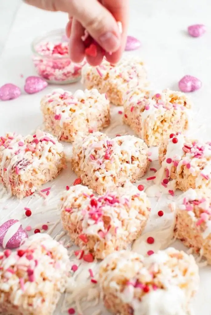 Heart-shaped rice crispy treats drizzled with white chocolate and sprinkled with colorful decorations, a playful and easy option for romantic desserts for two.