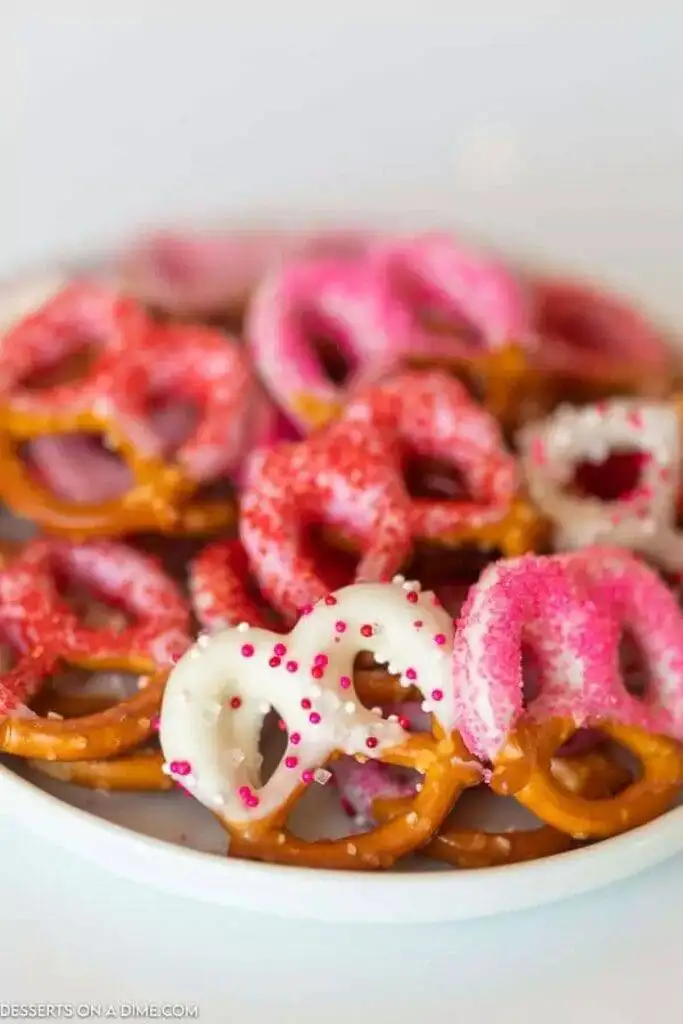A plate of colorful Valentine's Day pretzels, featuring a mix of plain and white chocolate-dipped pretzels sprinkled with pink and red decorations, perfect for festive treats or romantic desserts for two.