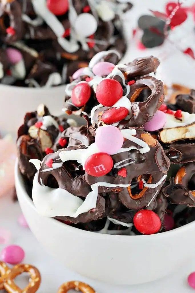 A bowl of festive Valentine's Day chocolate bark featuring a mix of dark chocolate, pretzels, red and pink M&M candies, and a drizzle of white chocolate, perfect for romantic desserts for two or sharing with loved ones.