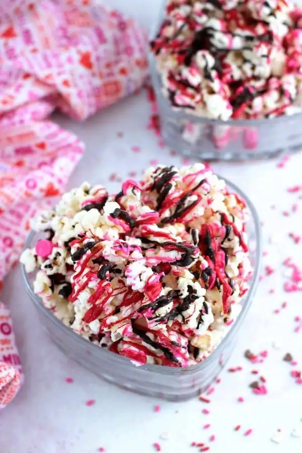 Heart-shaped bowls filled with popcorn drizzled in pink and chocolate icing, a sweet and playful idea for romantic desserts for two.