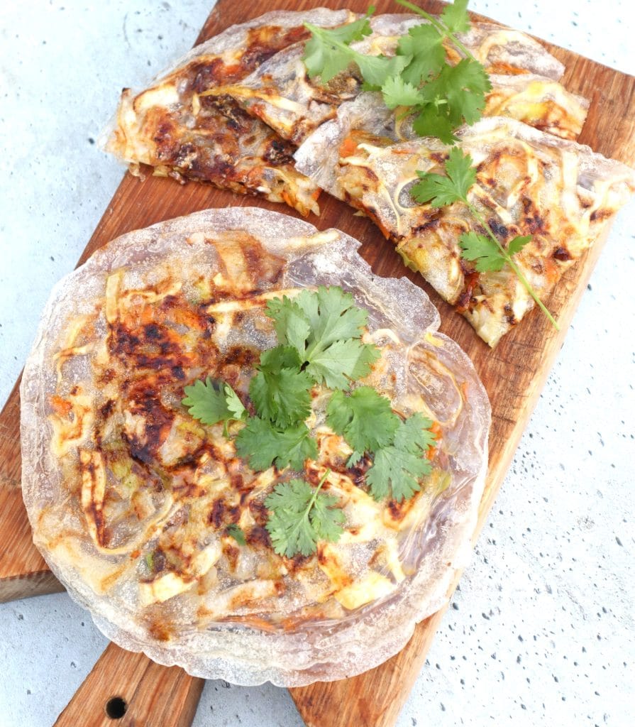 Crispy vegetable pancakes made with rice paper, filled with a mix of vegetables and cheese, garnished with fresh cilantro. Served on a wooden board, these unique and gluten-free pancakes are a creative option for Superbowl appetizers or light snacks.
