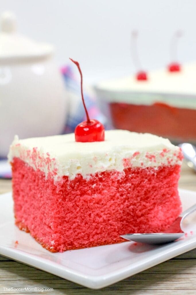 Close-up of a vibrant pink cake slice topped with creamy white frosting and a cherry, perfect for Valentine's Cake Ideas, showcasing a festive and romantic dessert option.