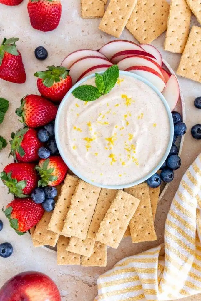 Light and creamy fruit dip topped with lemon zest, served with fresh berries, apple slices, and graham crackers—a sweet addition to the best party dips spread.
