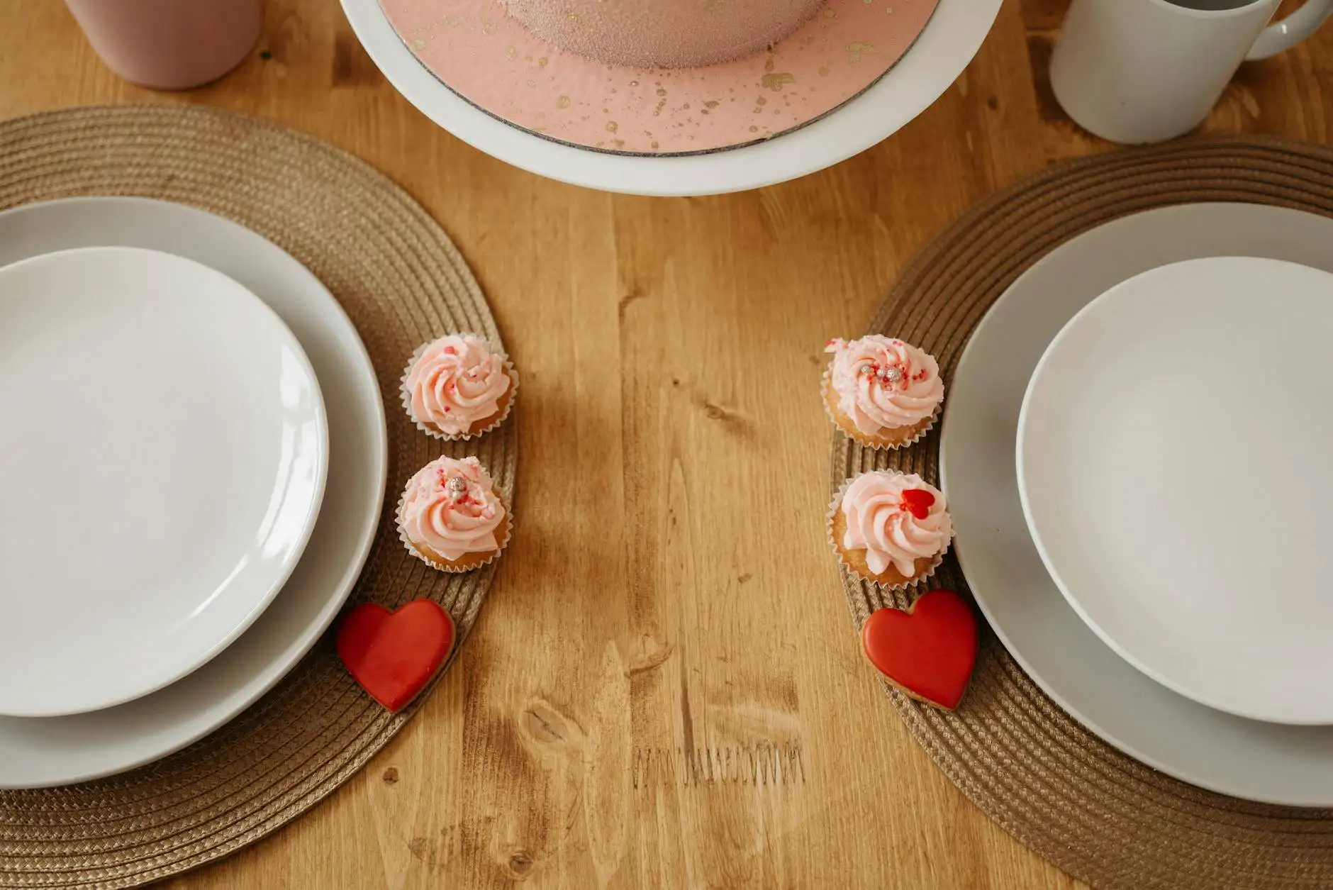Romantic table setting for two with pink frosted cupcakes and heart-shaped decorations, ideal for enjoying romantic desserts for two.