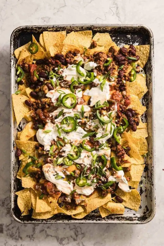 Loaded Irish-inspired nachos topped with seasoned ground beef, kidney beans, fresh jalapeños, sour cream, and green onions, making them a bold and flavorful Irish party food!