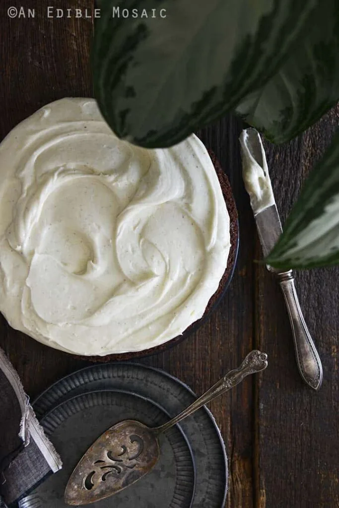 A rich chocolate cake topped with creamy vanilla frosting, styled on a rustic wooden table with vintage plates and utensils, perfect for Irish desserts or St. Patrick's Day celebrations.