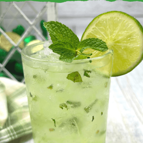 A refreshing green mojito served in a frosted glass, filled with ice, muddled mint leaves, and garnished with a lime slice and fresh mint sprig, set against a festive backdrop with green accents.