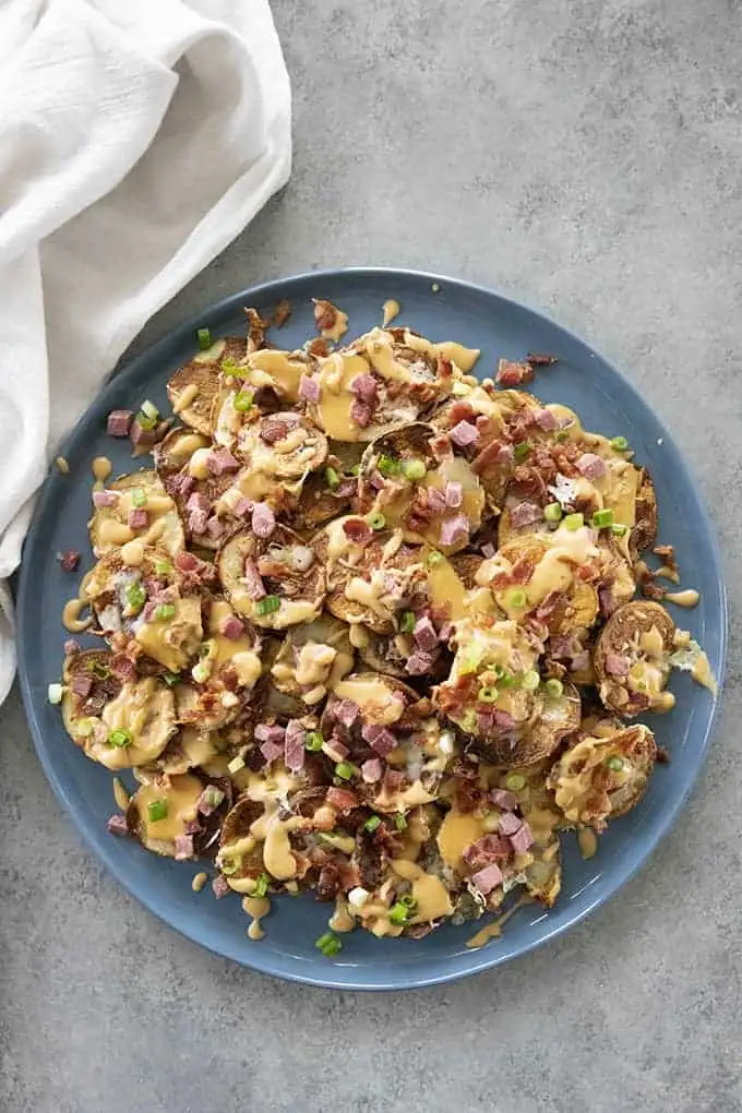 A vibrant plate of crispy Irish potato nachos, topped with melted cheese, diced ham, green onions, and a drizzle of creamy sauce—a perfect Irish party food appetizer!